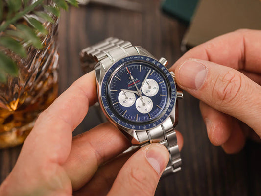 Omega speedmaster watch being held in a person's hand. The person is either setting time on his watch or manually winding it by rotating the crown of the watch.